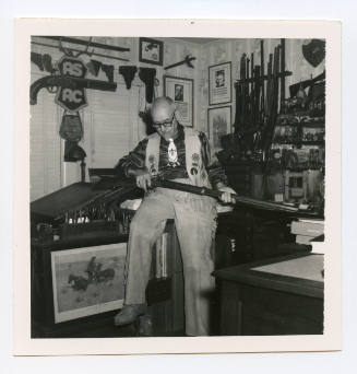 Herschel C. Logan in his study posing with a rifle